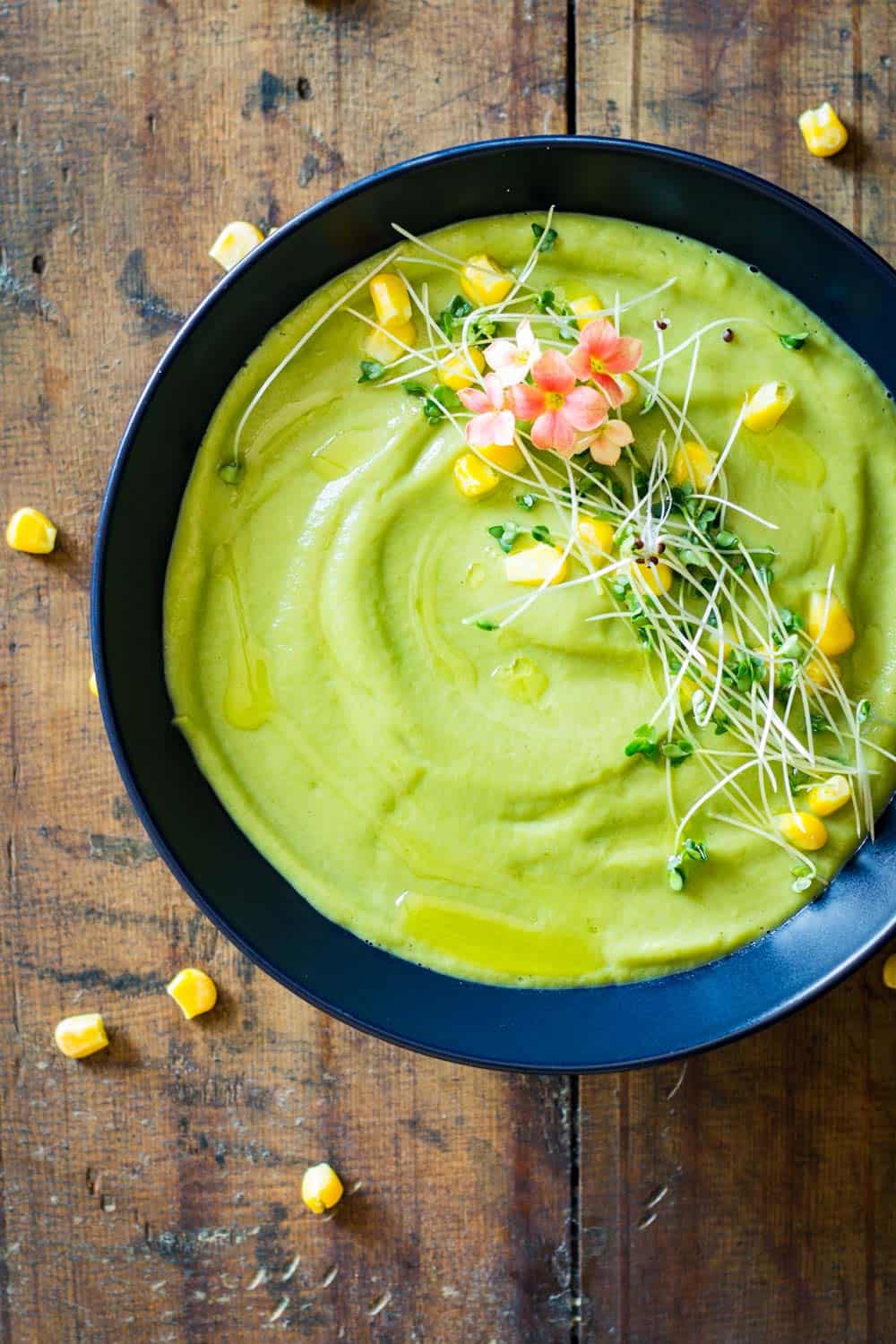 Vegan Cream Broccoli Soup garnished with fresh herbs, flowers and corn kernels.