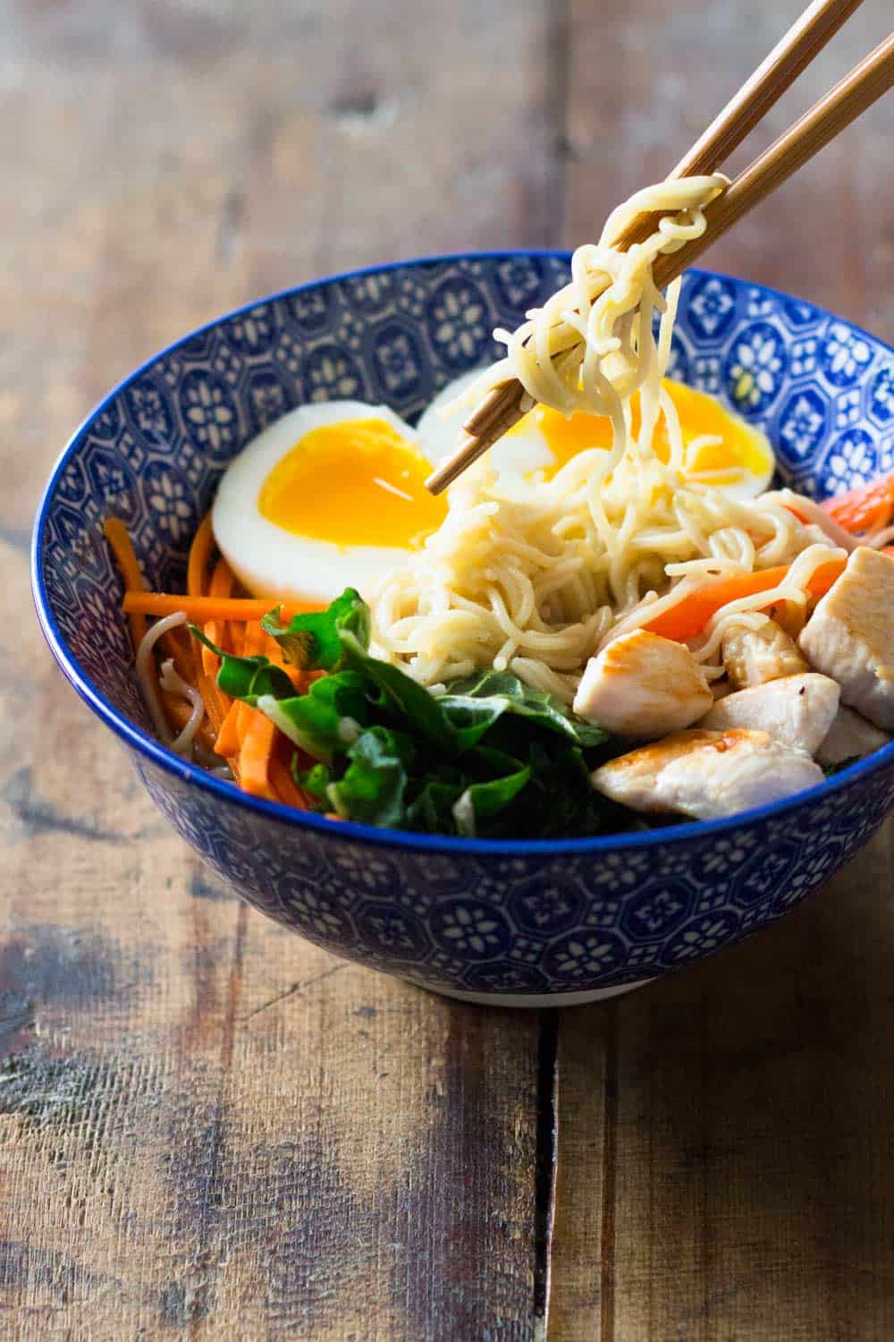 Bowl of ramen chicken noodle soup, with chopsticks lifting some noodles. 