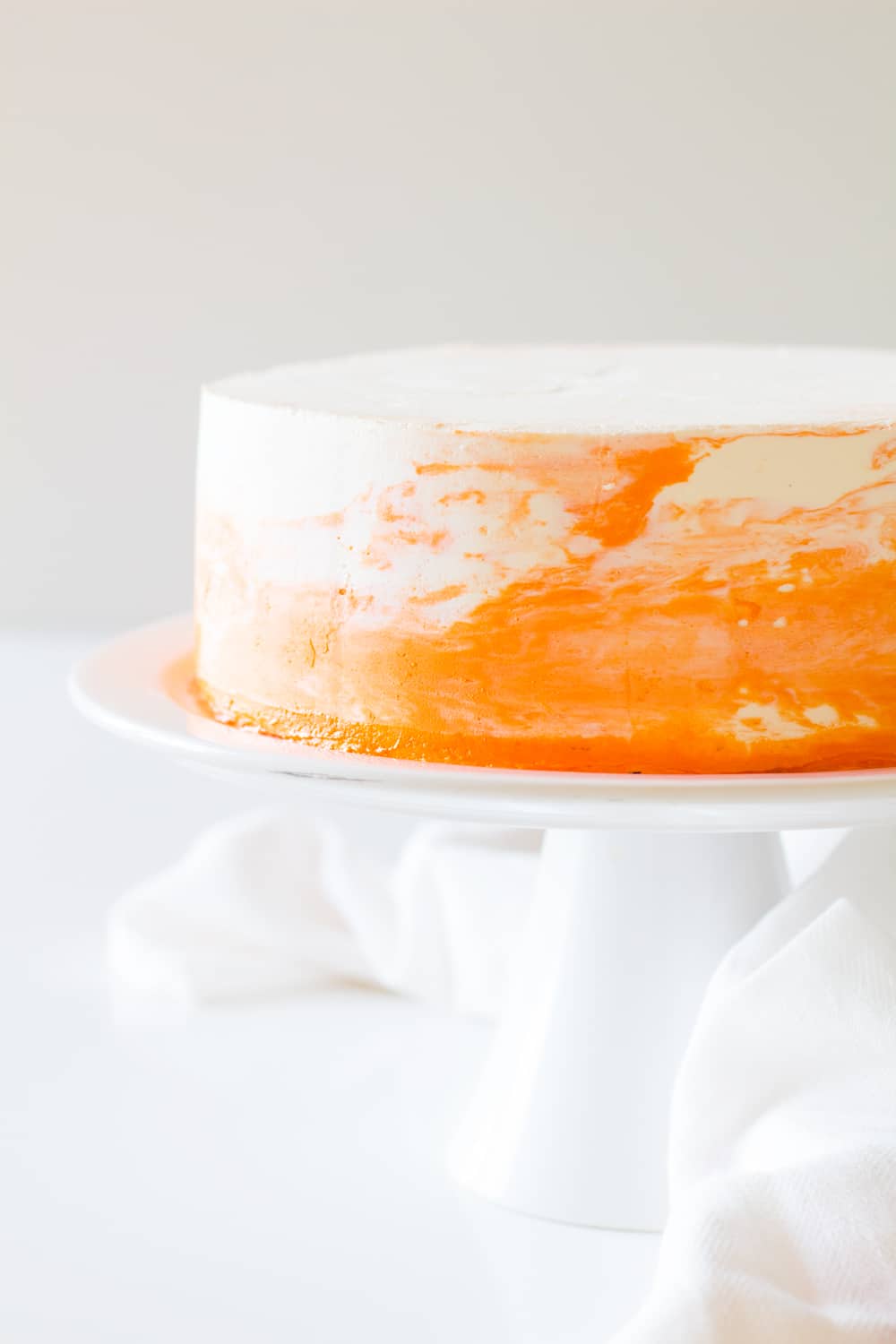 Vanilla cake with white and orange coconut cream frosting on a white cake stand.