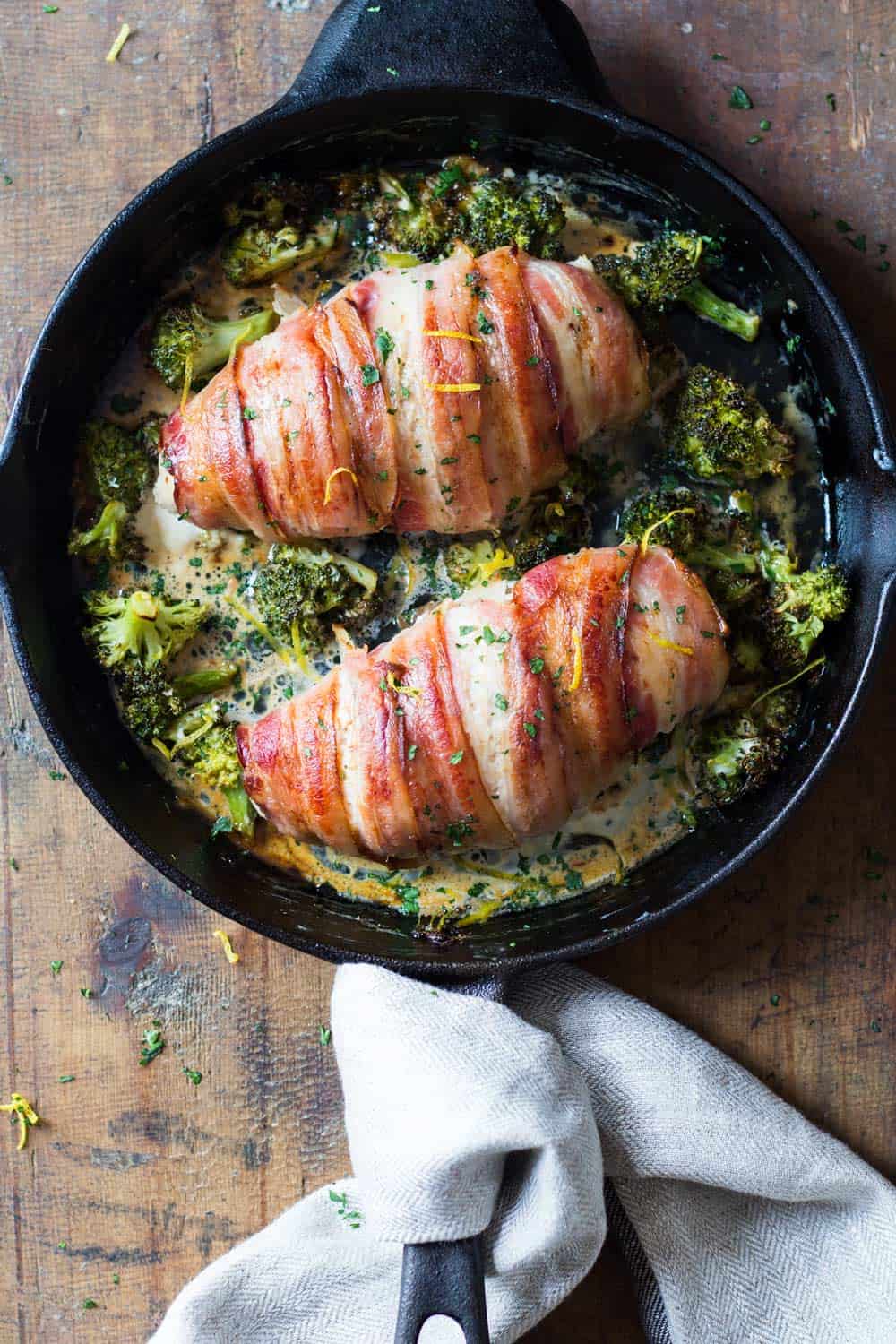 Top down view of baked bacon-wrapped chicken breast in black pan with broccoli