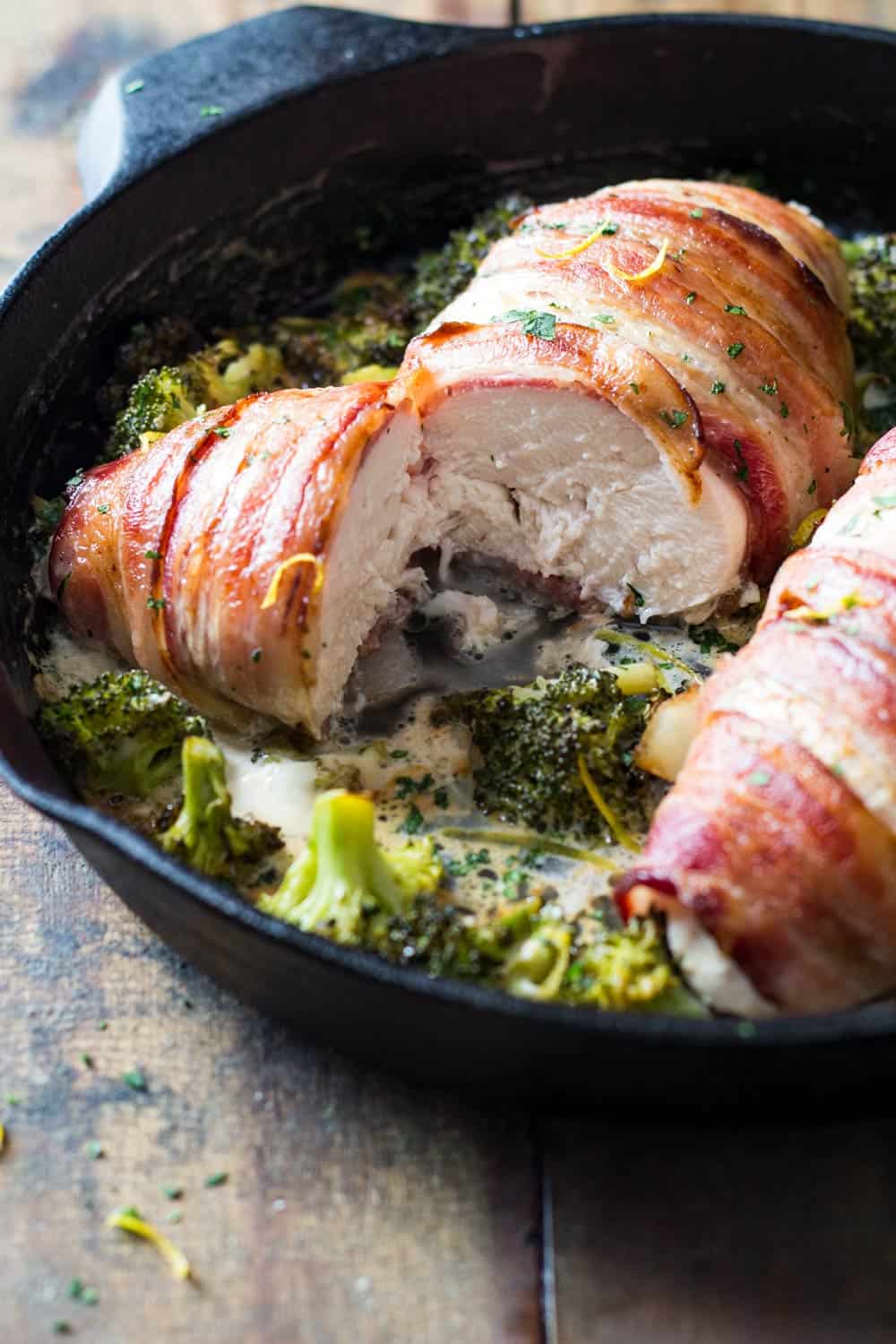 Close up view of texture of chicken breast with bacon and broccoli in cast iron skillet.