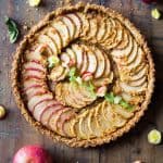 Top down view of baked apple tart on a rustic wood board and fresh apples.