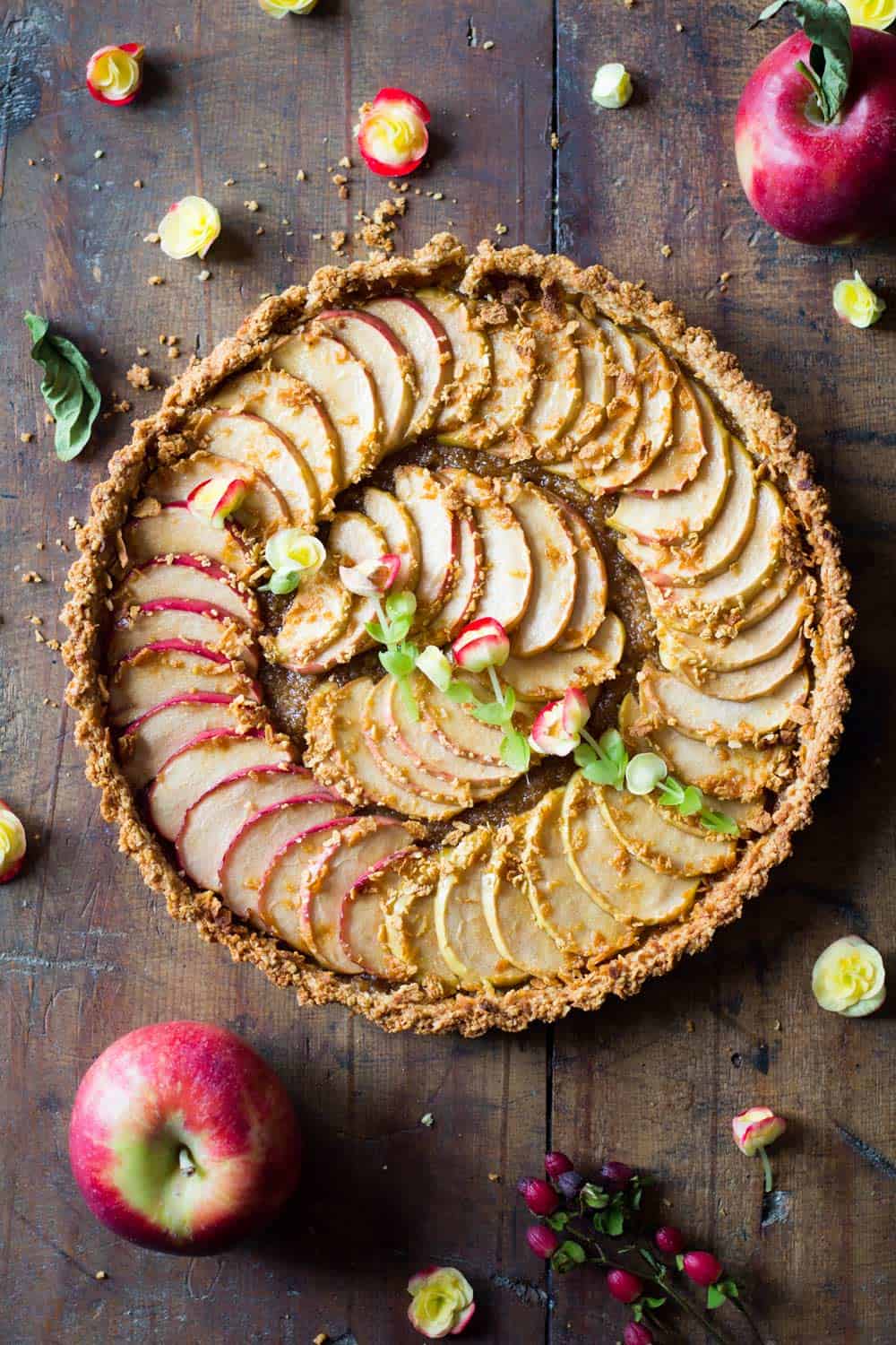 Top down view of baked apple tart on a rustic wood board and fresh apples.