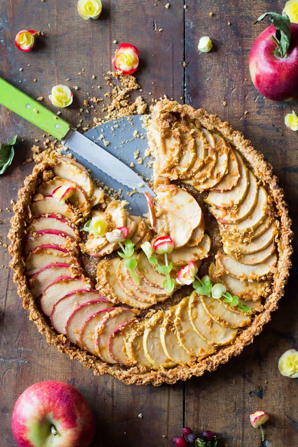 Top down view of baked apple tart missing a slice, and a cutting knife. 