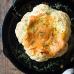 Whole roasted cauliflower with melted cheese in a cast iron pan.