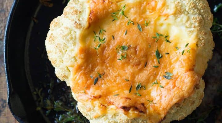 Whole roasted cauliflower with melted cheese in a cast iron pan.