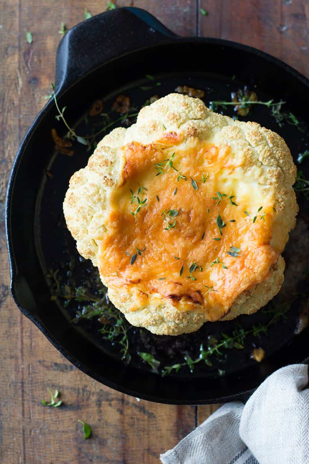 Whole roasted cauliflower with melted cheese in a cast iron pan.