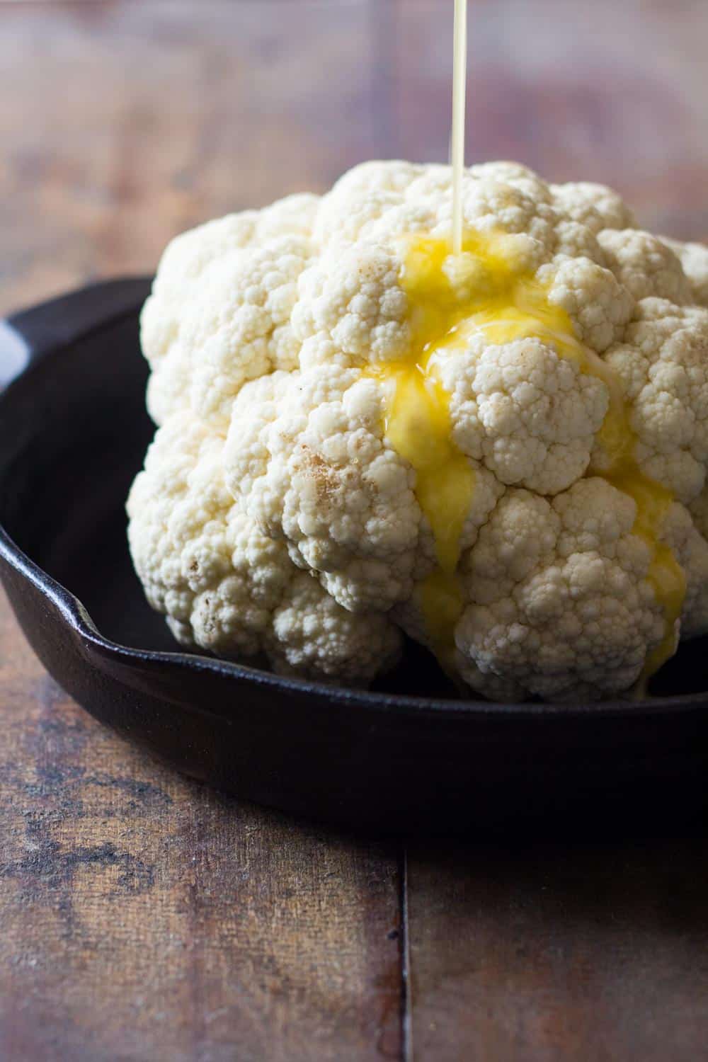 Melted butter being poured over whole head of cauliflower before roasting. 