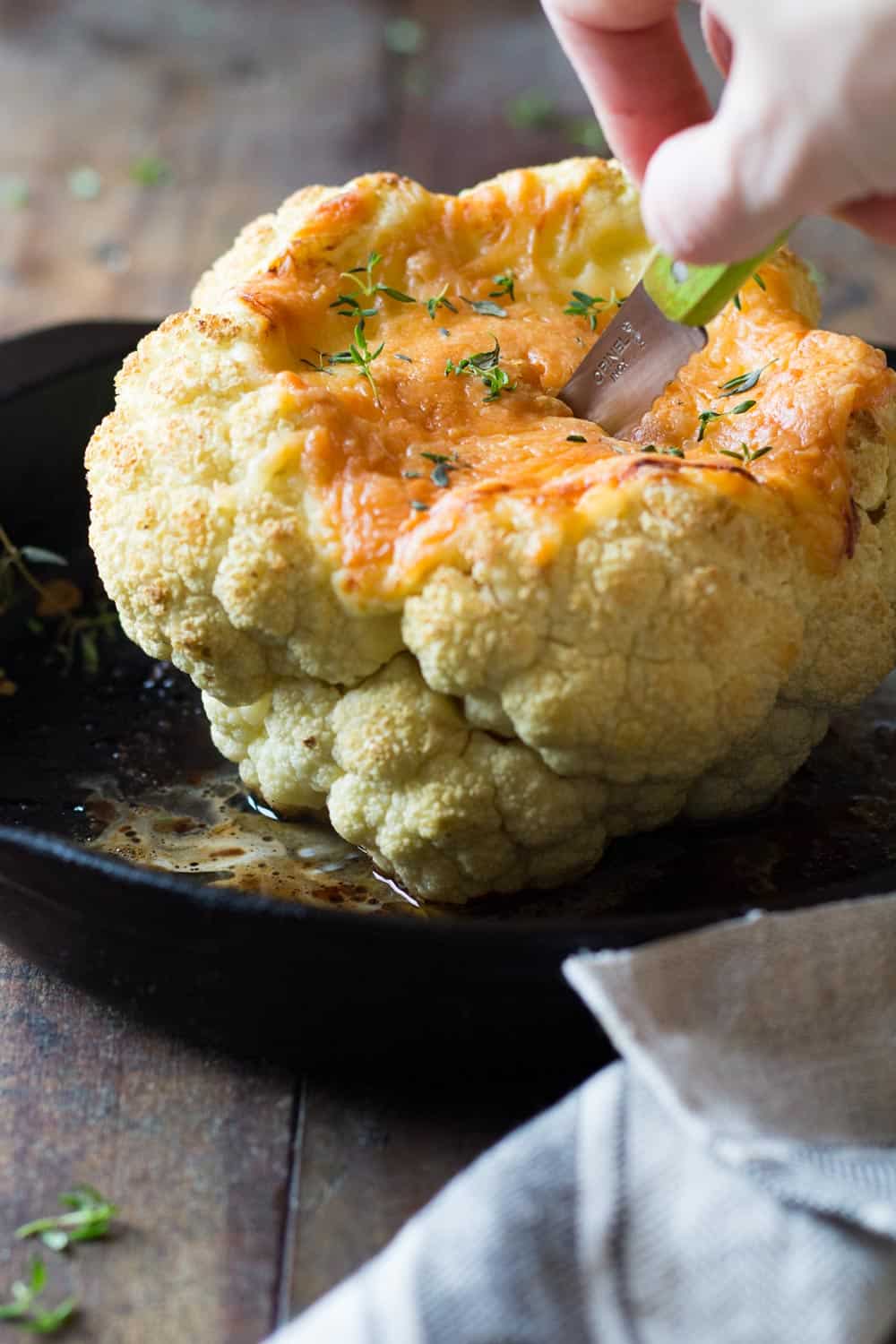 Knife inserted in head of roasted cauliflower with melted cheese. 