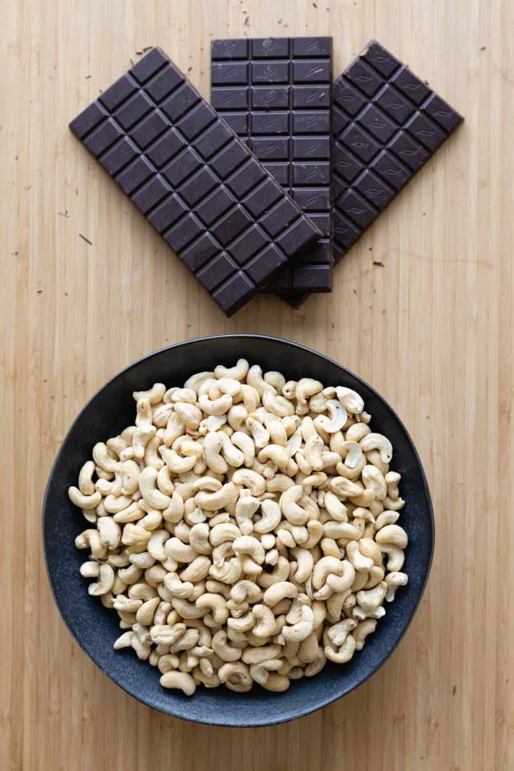 A bowl full of cashews and 3 chocolate bars on a kitchen counter.