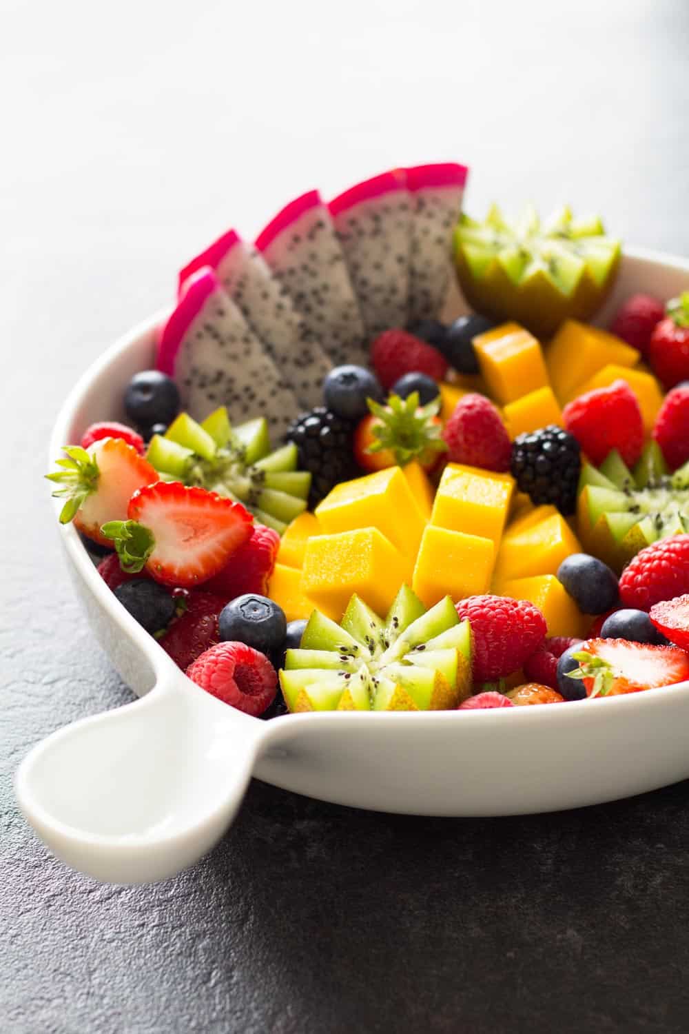 Fruit platter presented in a white bowl with a handle. 