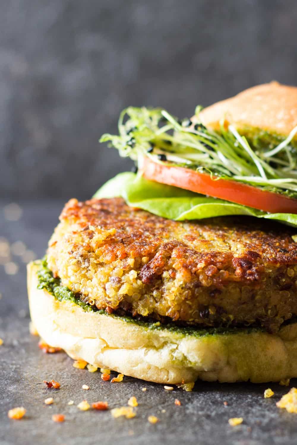 Detail of quinoa veggie burger to show texture, in a bun with lettuce, tomato, micro greens and basil pesto sauce. 