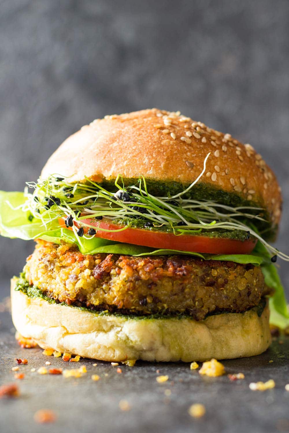 Side view of quinoa burger in a bun with lettuce, tomato, micro greens and basil pesto sauce. 