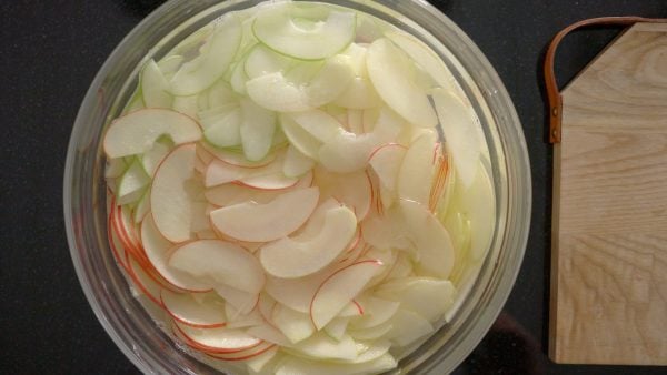 Apple slices in water in a big bowl.