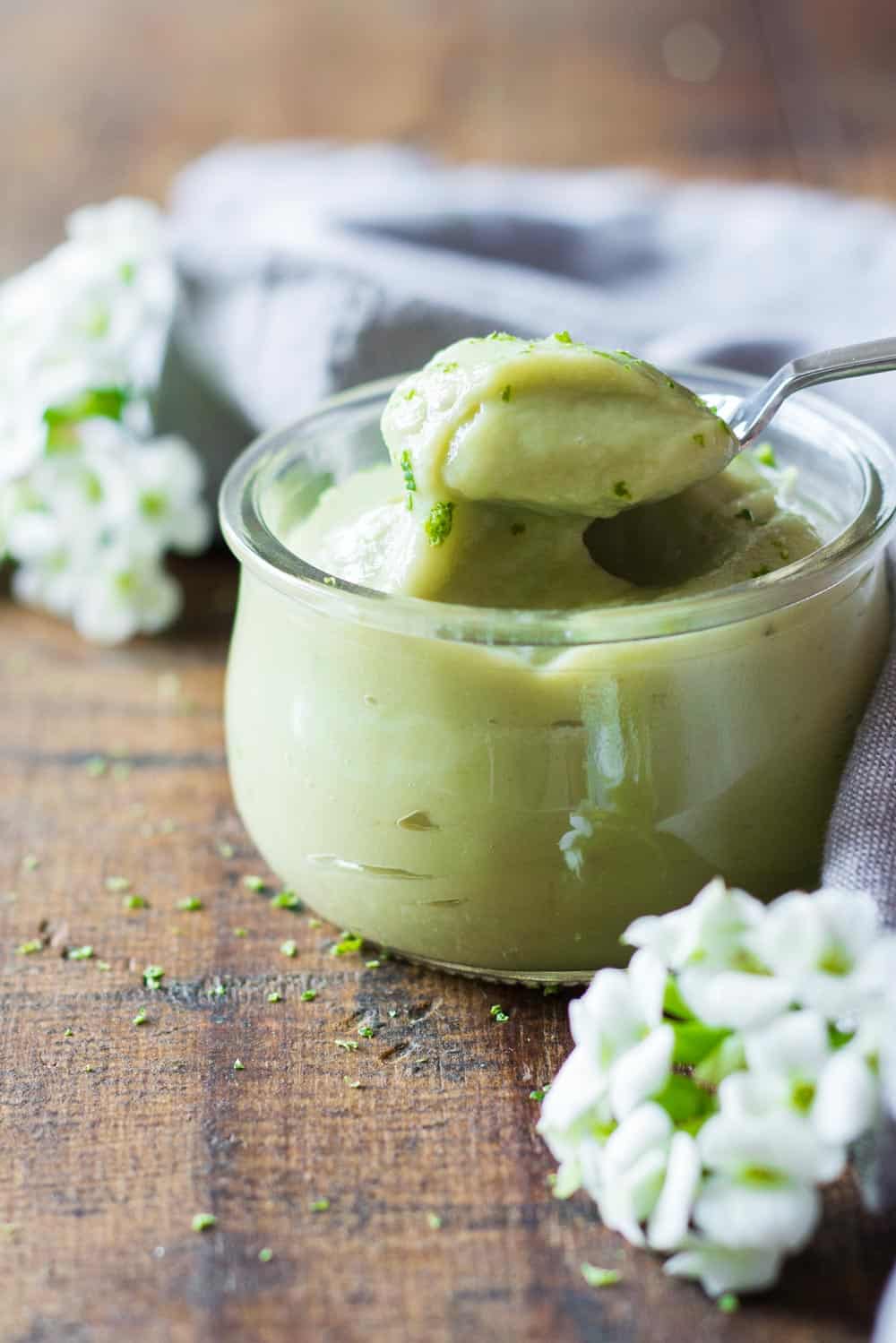 Spoonful of key lime pudding being grabbed from a glass jar. 