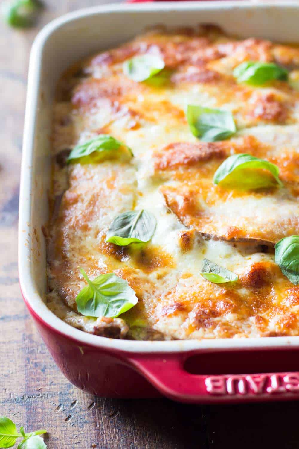 Detail of baked sweet potato lasagna topped with fresh basil leaves, in a red baking dish.