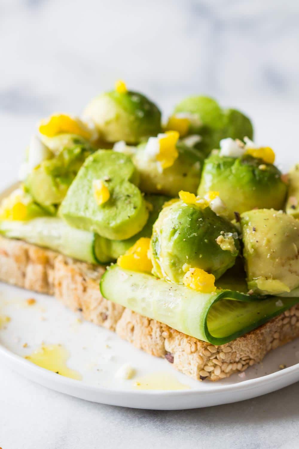 Avocado toast with zucchini slices and poached egg served on a white plate. 