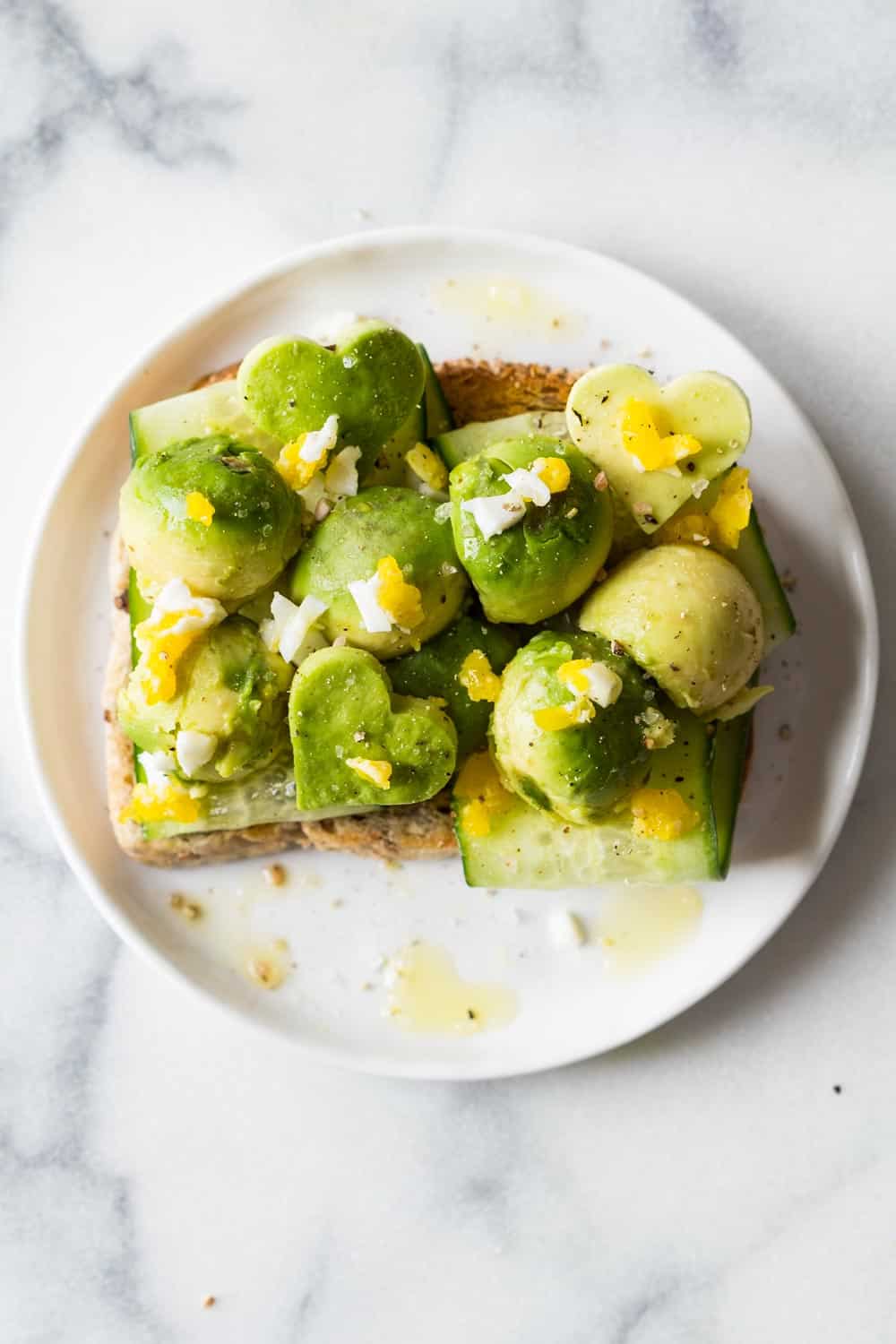 Top view of avocado toast with zucchini slices and chopped poached egg, served on a white plate.