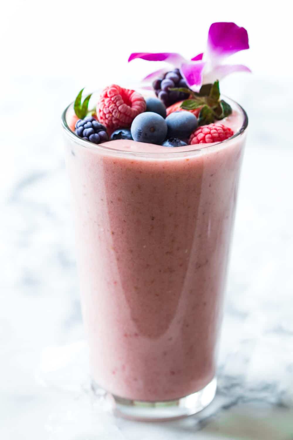 Glass of strawberry banana smoothie without yogurt filled to the rim, topped with raspberries, blueberries, blackberries and strawberries.