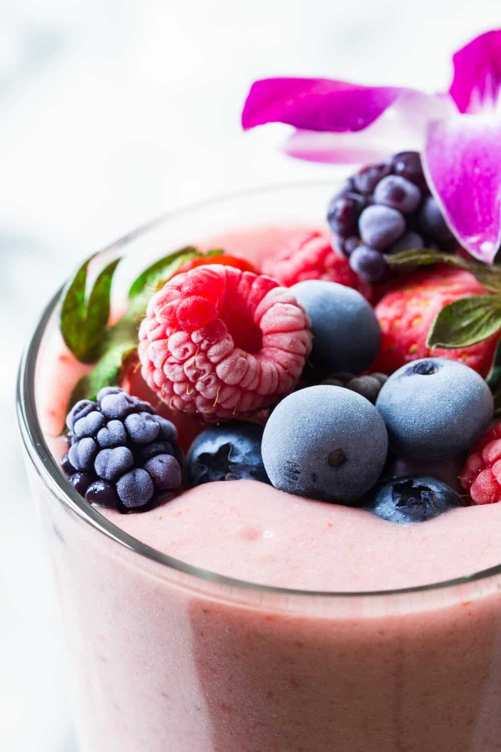 Close up of glass of strawberry smoothie to show texture of topping fruits, blackberries, raspberries, blueberries and strawberries.