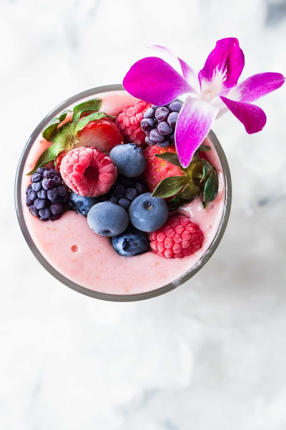 Top view of strawberry banana smoothie without yogurt, topped with raspberries, blueberries, strawberries and blackberries. 
