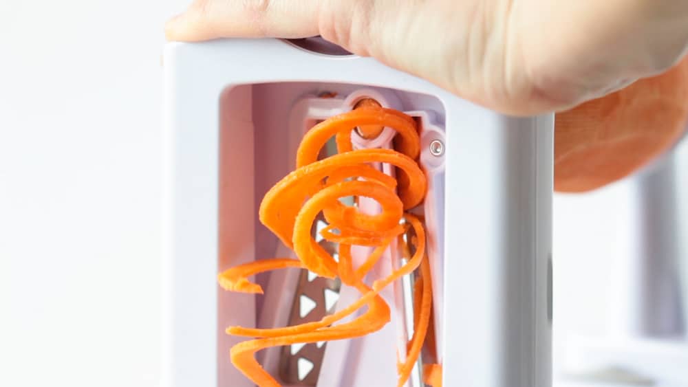 Two hands holding a spiralizer making sweet potato noodles. 