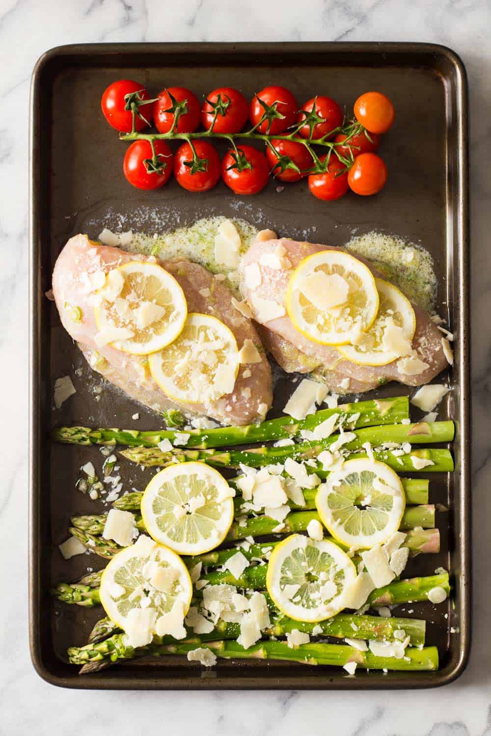 Sprig of cherry tomatoes, lemon chicken breasts and asparagus in a pan. 