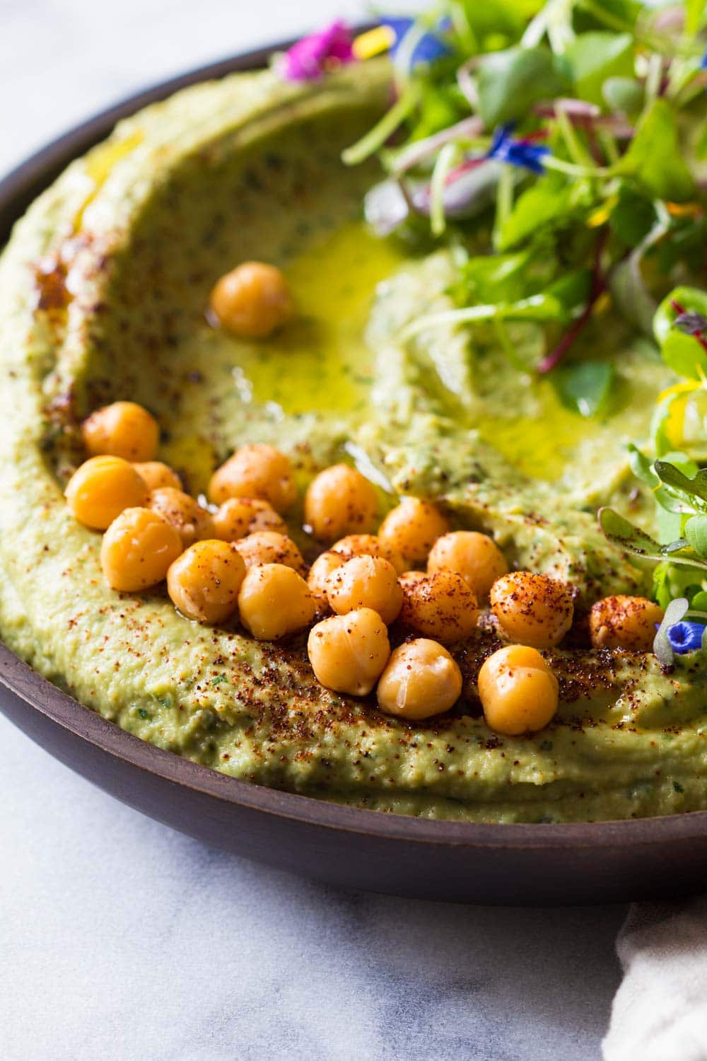 Spicy hummus and avocado presented in a bowl with whole chickpeas and lettuce leaves, sprinkled with chili powder. 