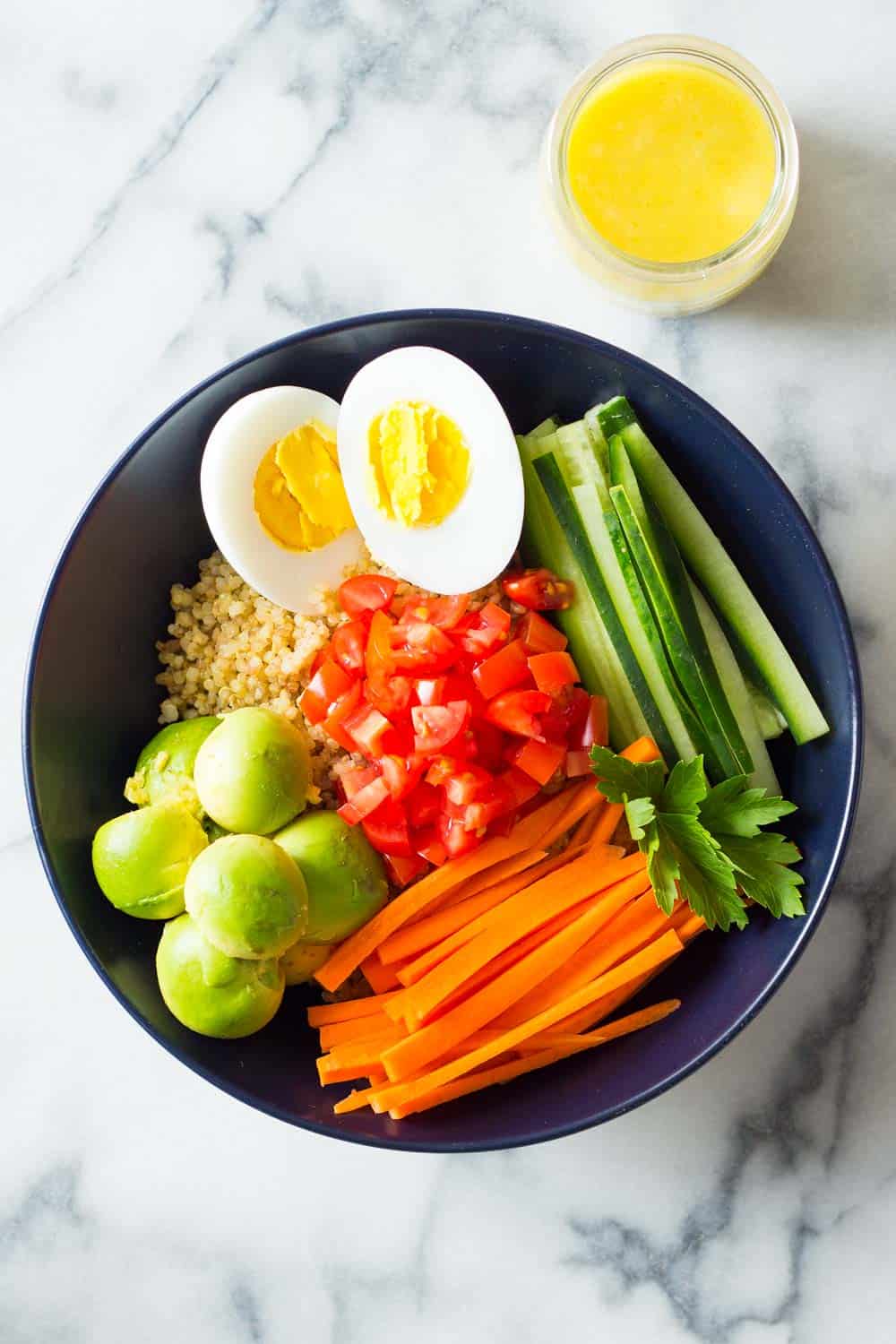 Instant Pot Quinoa Bowl with hard-boiled egg, cucumber, carrots, tomatoes, avocado and lemon tahini dressing.