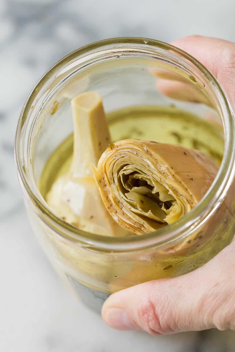 Close up of a hand holding an open artichoke hearts jar. 