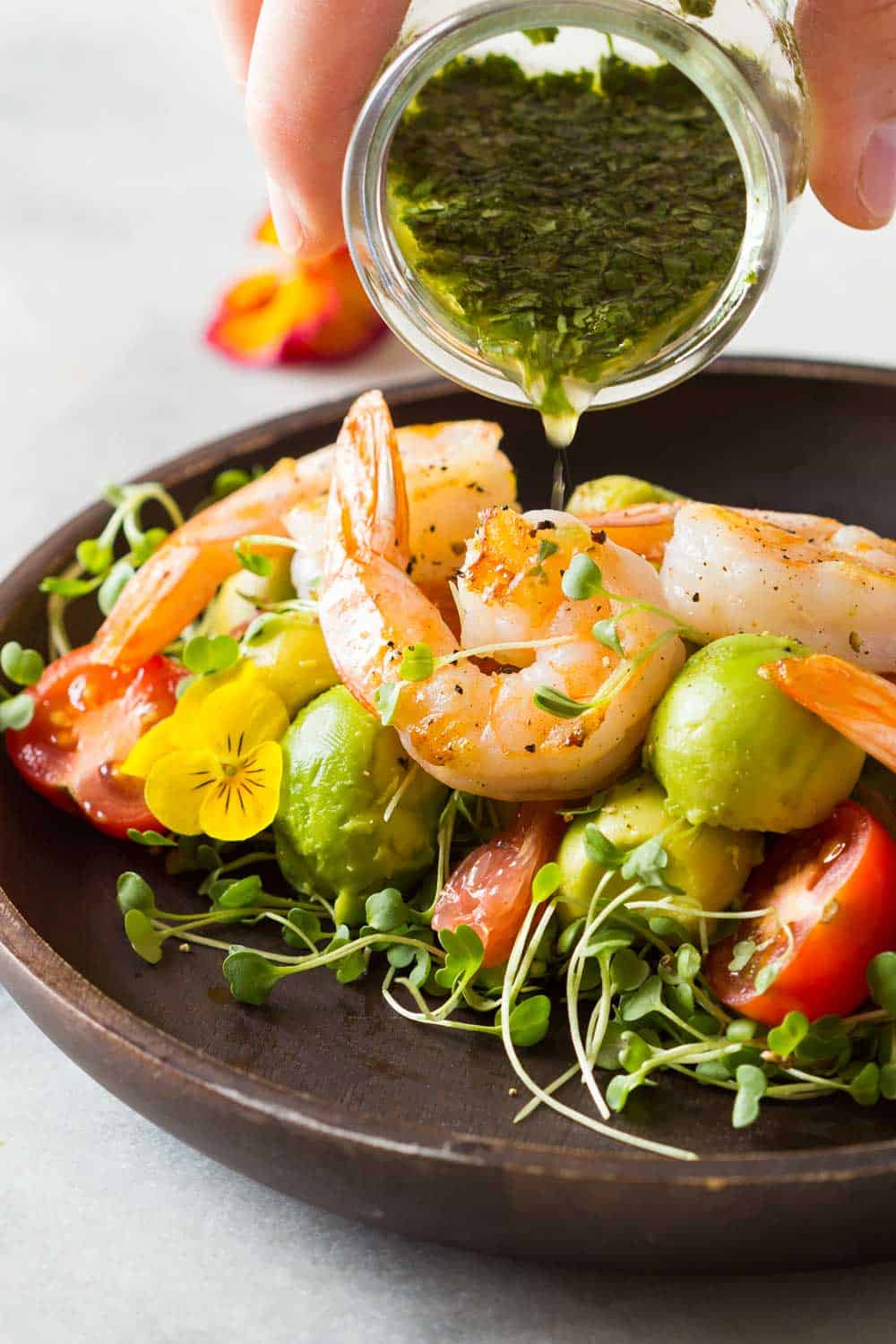 Shrimp, avocado, tomato, arugula and grapefruit on a plate with cilantro dressing being poured on it.