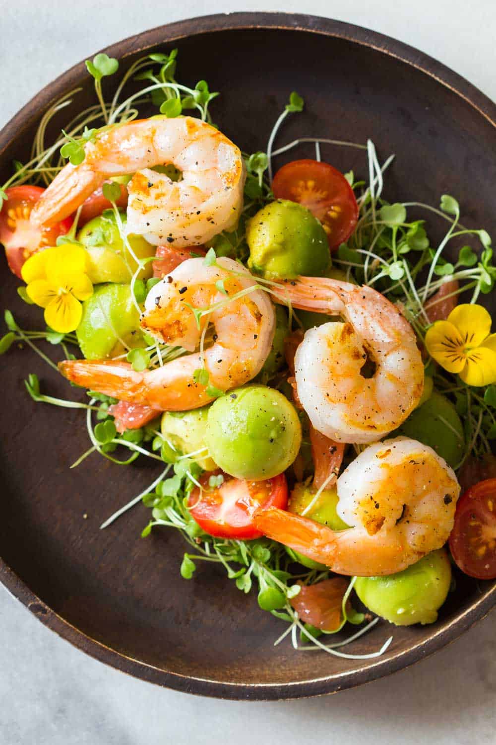 Shrimp, avocado, tomato, arugula and grapefruit with cilantro dressing served on a brown bowl.