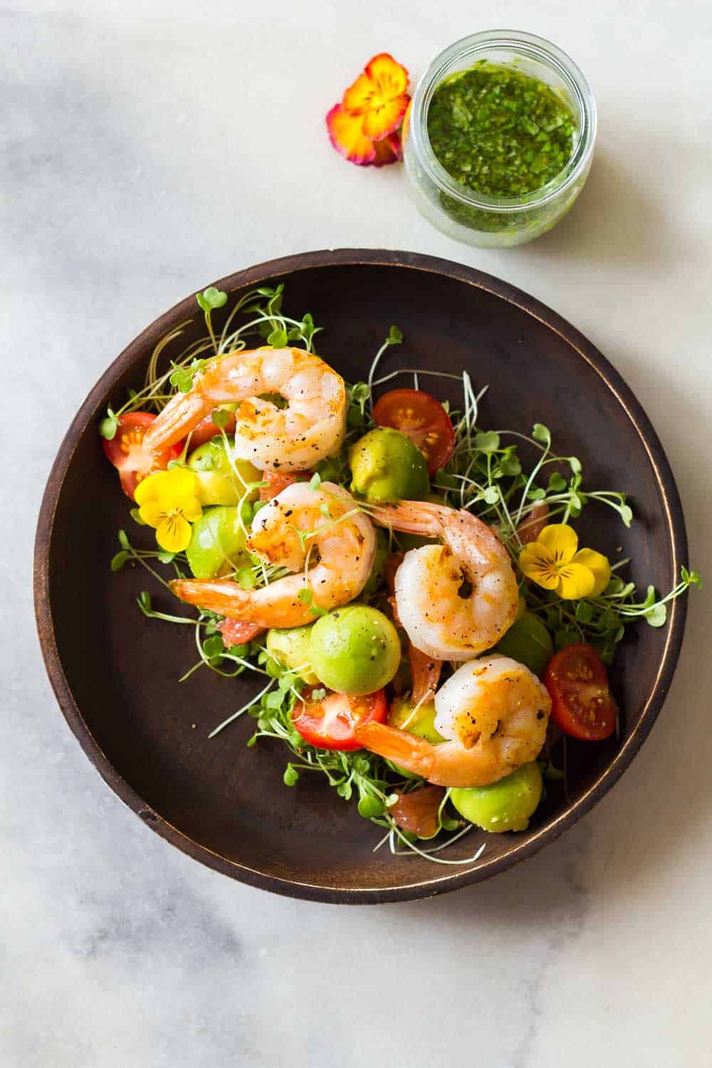 Shrimp, avocado, tomato, arugula and grapefruit on a plate with cilantro dressing in a jar.