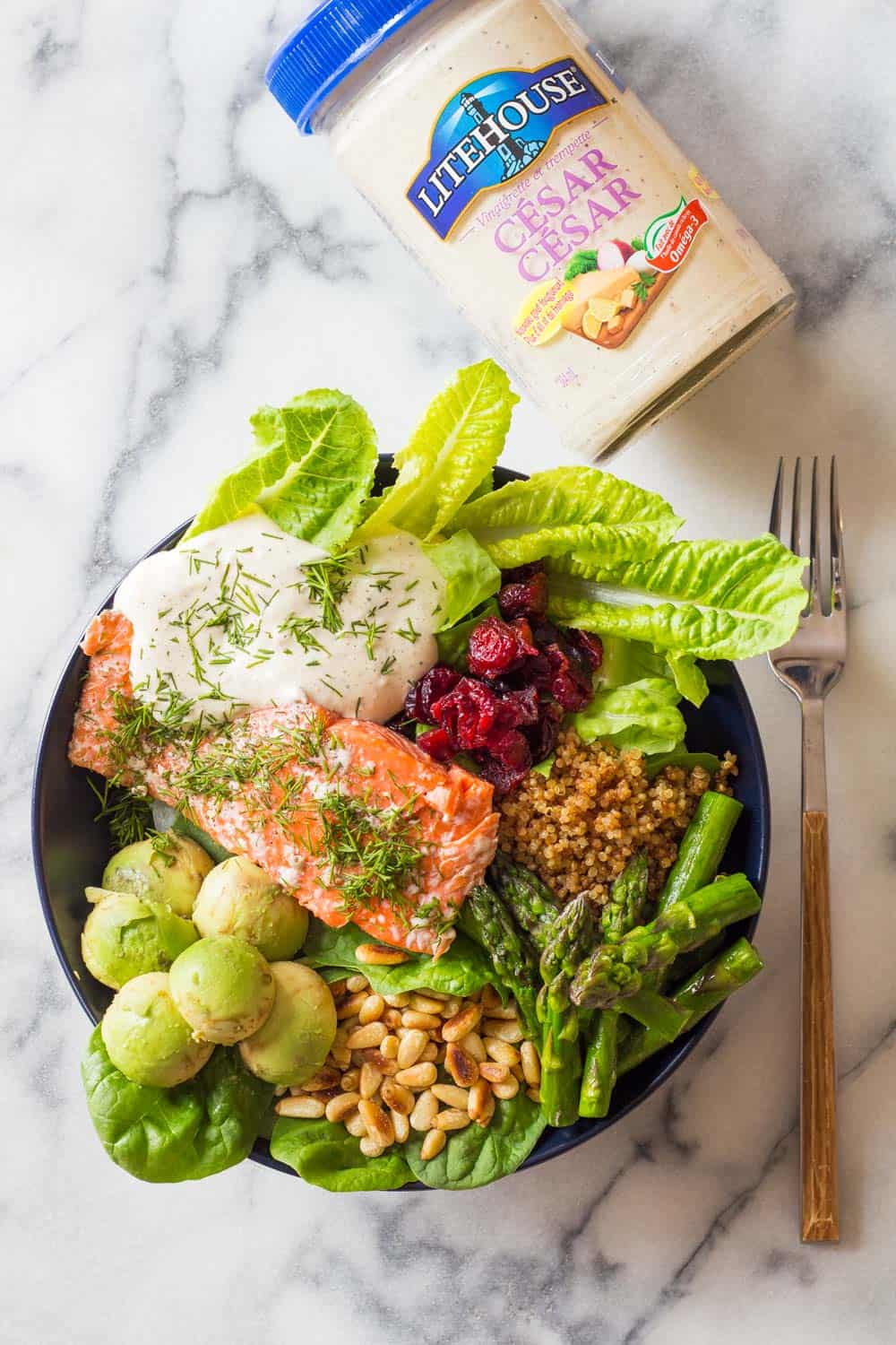 Top view of Sockeye Salmon salad in a plate with a fork, and a bottle of Litehouse Cesar dressing on top. 