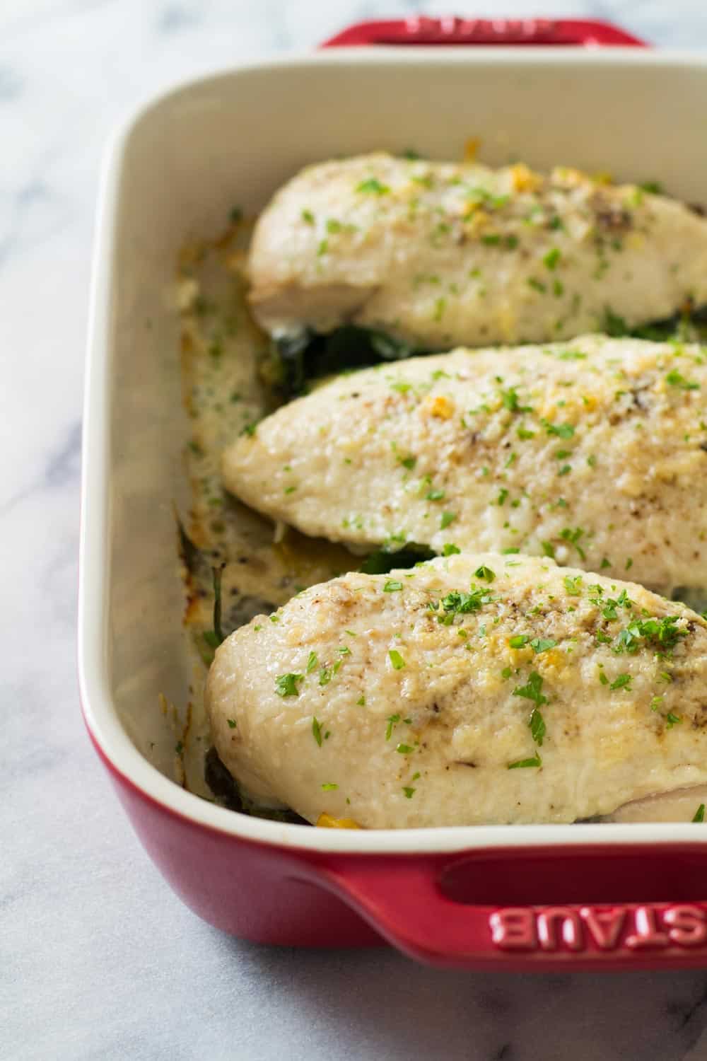 Baked spinach artichoke chiken breasts in a red baking dish. 