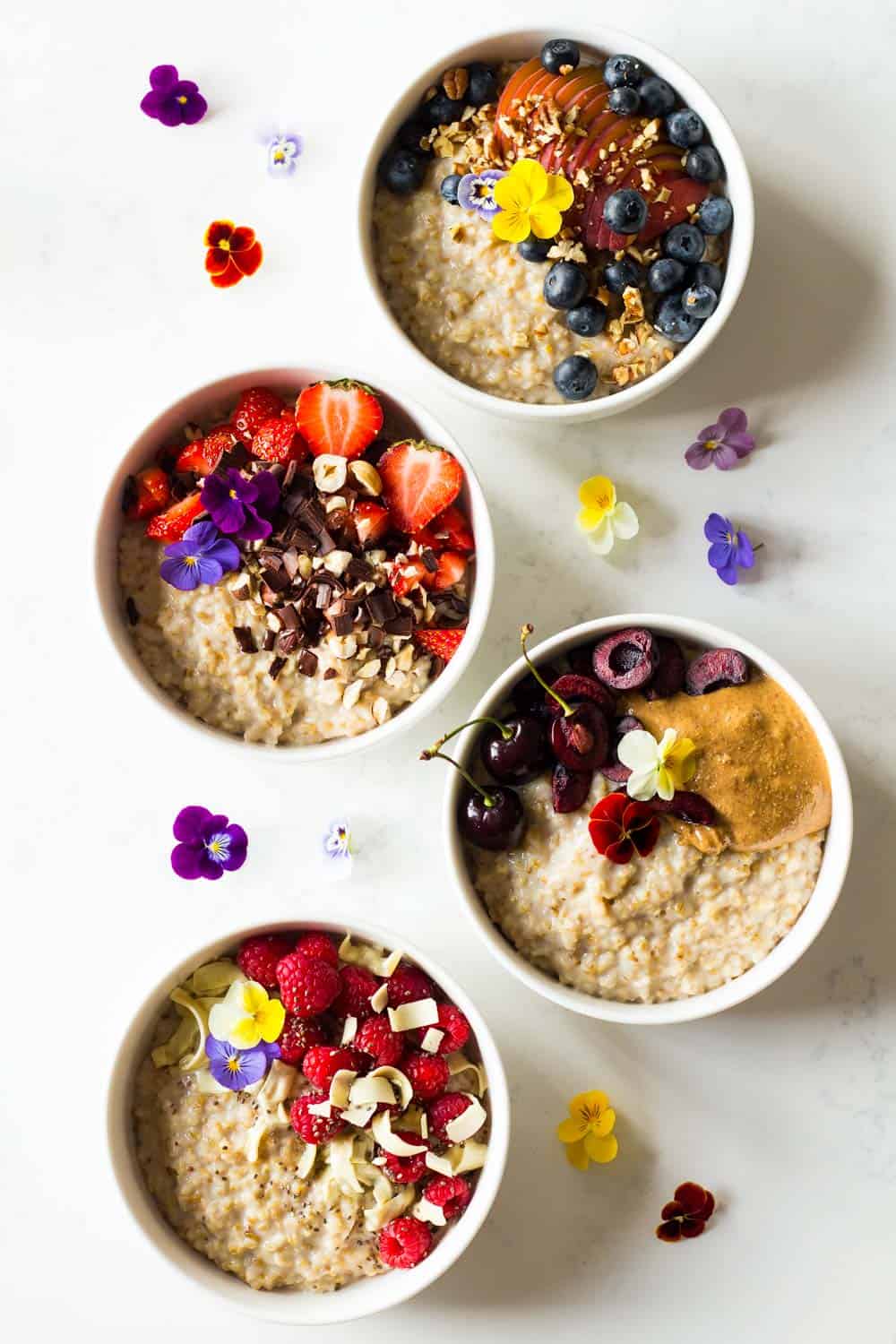 Four Instant Pot Steel Cut Oats bowls with different toppings, garnished with fresh flowers.