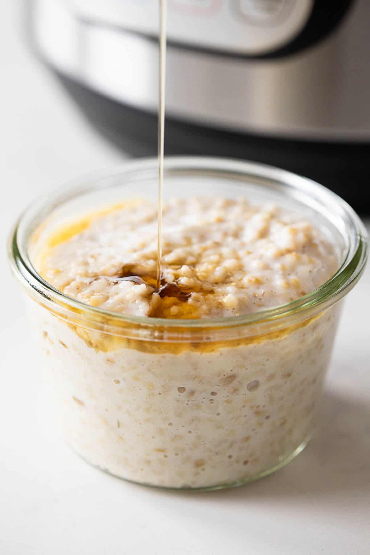 An Instant Pot in the background and cooked steel cut oats in a jar in front.