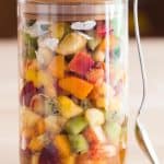 Mango Fruit Salad in a jar with a spoon leaning against it.