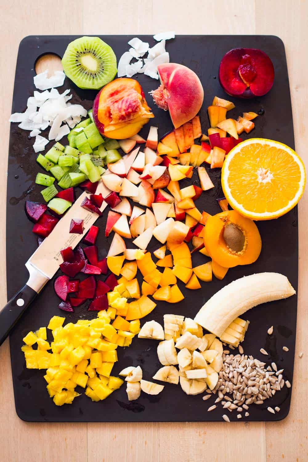 Ingredients for a mango fruit salad - mango, banana, stone fruit, kiwi, seeds, dried coconut