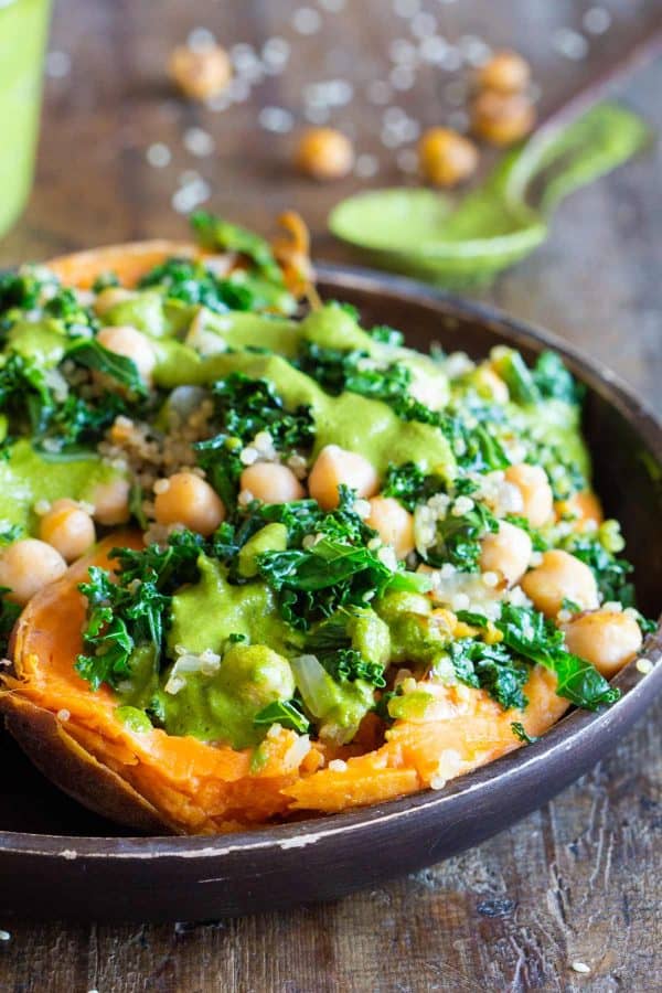 kale chickpea quinoa stuffed sweet potato with green sauce on a wooden plate