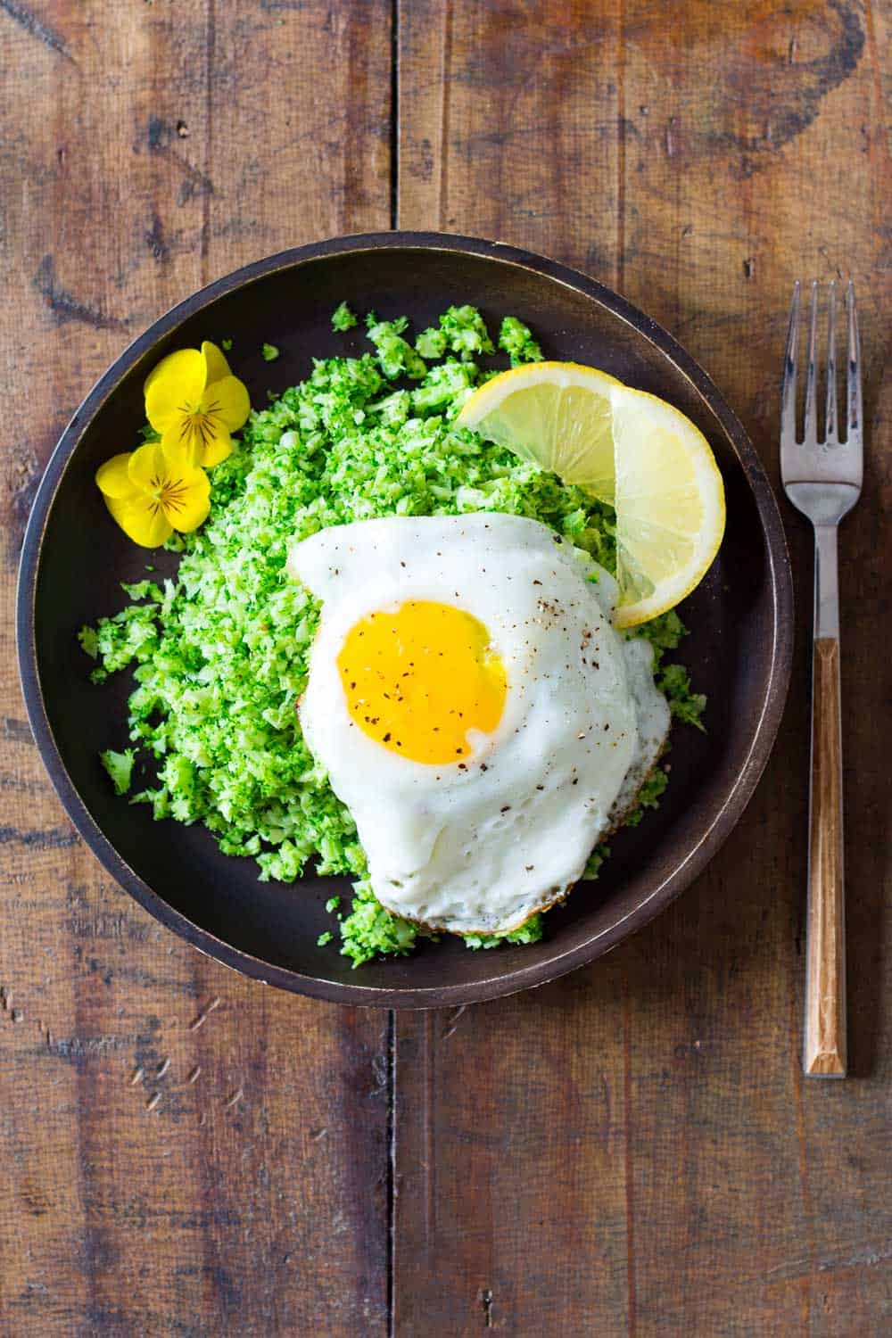 Broccoli rice served on a wooden plate, topped with a fried egg and lemon slices