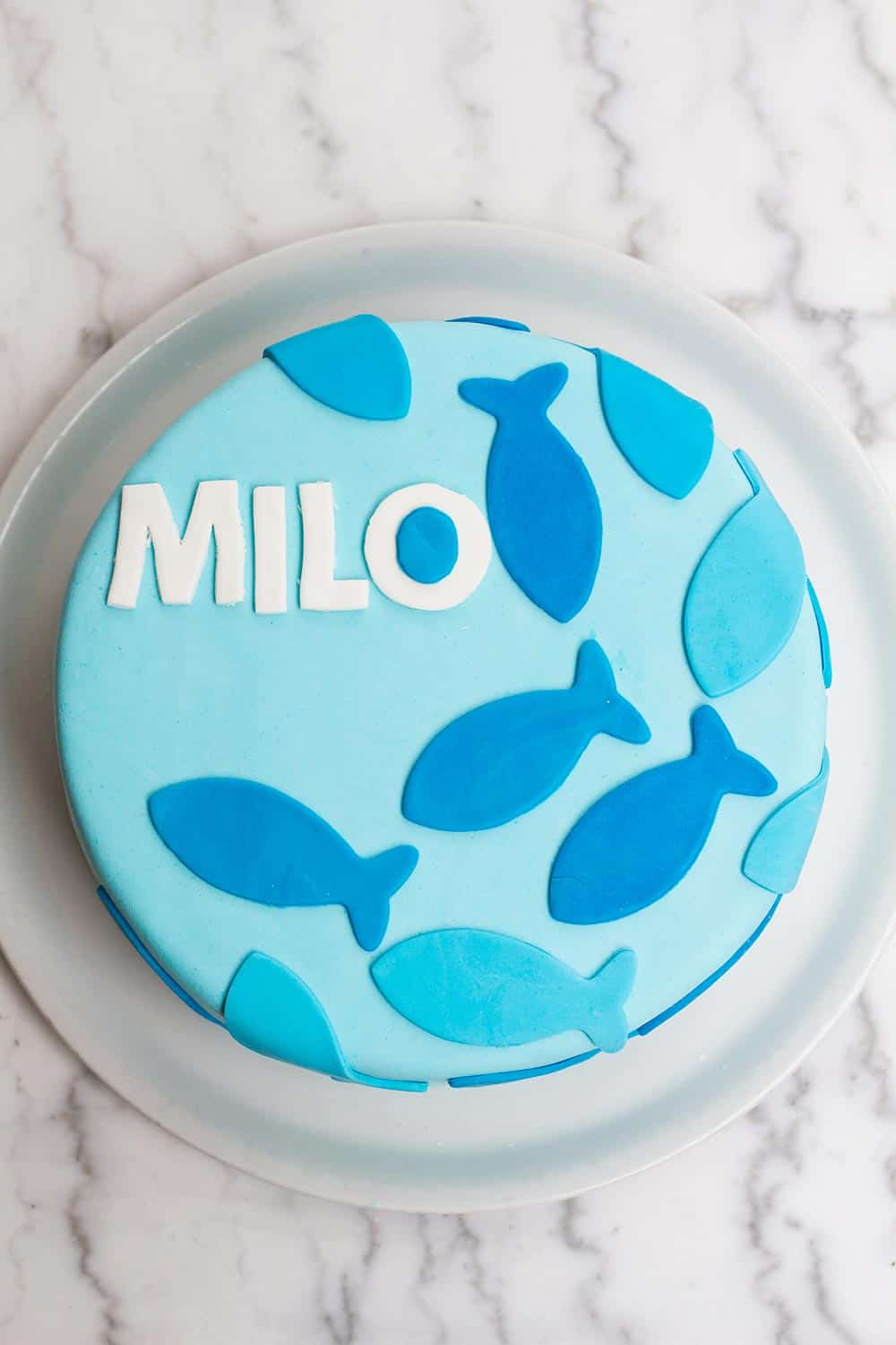 A blue cake decorated with blue frosting fish and the name Milo.