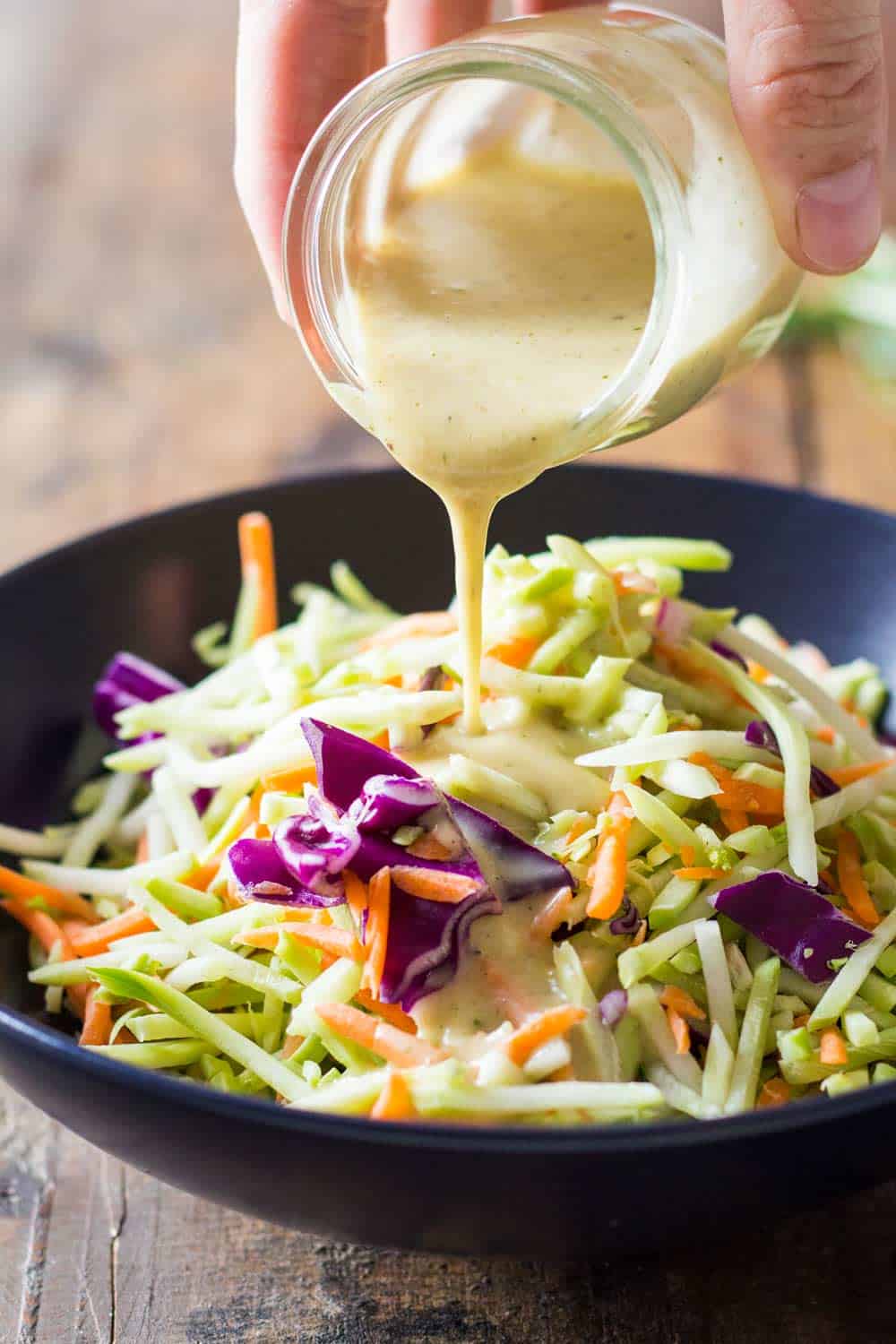 Broccoli Slaw Dressing being poured over slaw served on a black plate