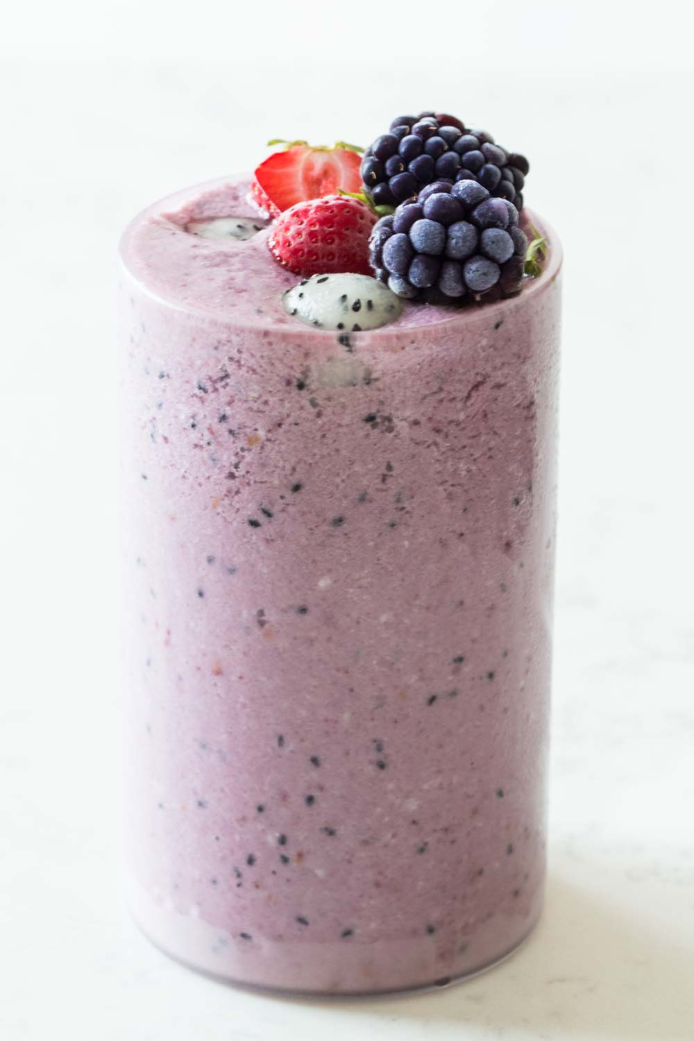 Tall glass filled to the rim with dragon fruit smoothie topped with strawberries, blackberries and balls of dragon fruit