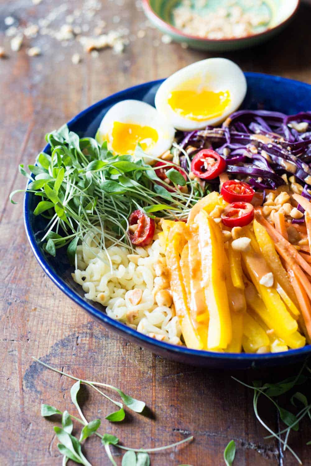 Ramen noodle salad with veggies and soft-boiled egg topped with peanut sauce, presented in a blue plate