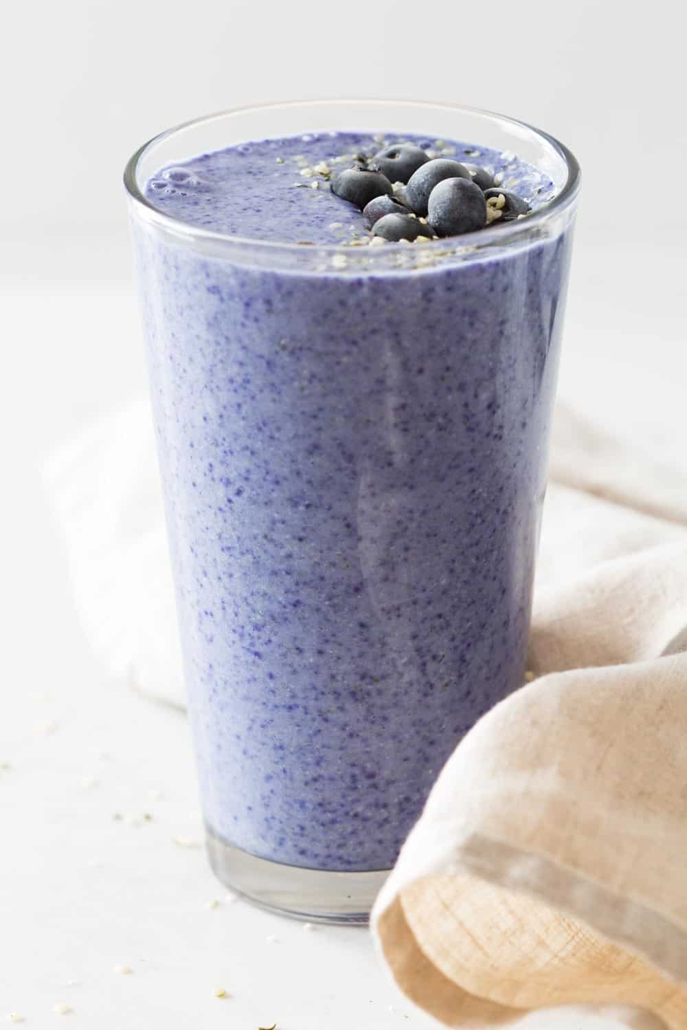 blue purple smoothie in a tall glas with blueberries on top