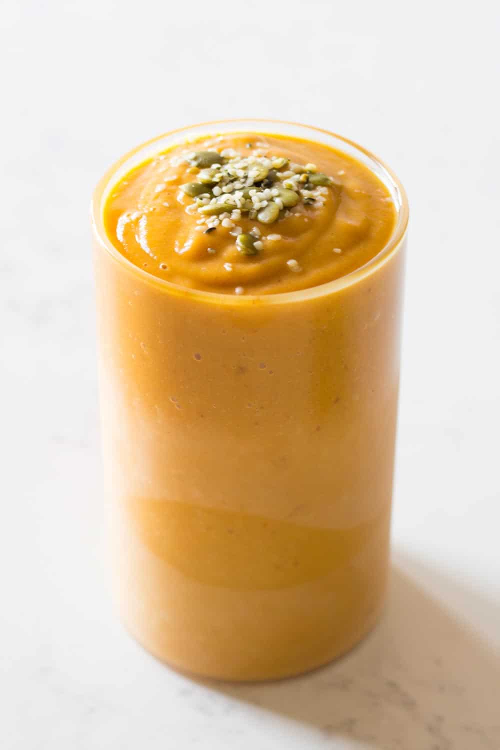 pumpkin smoothie in a glass topped with seeds
