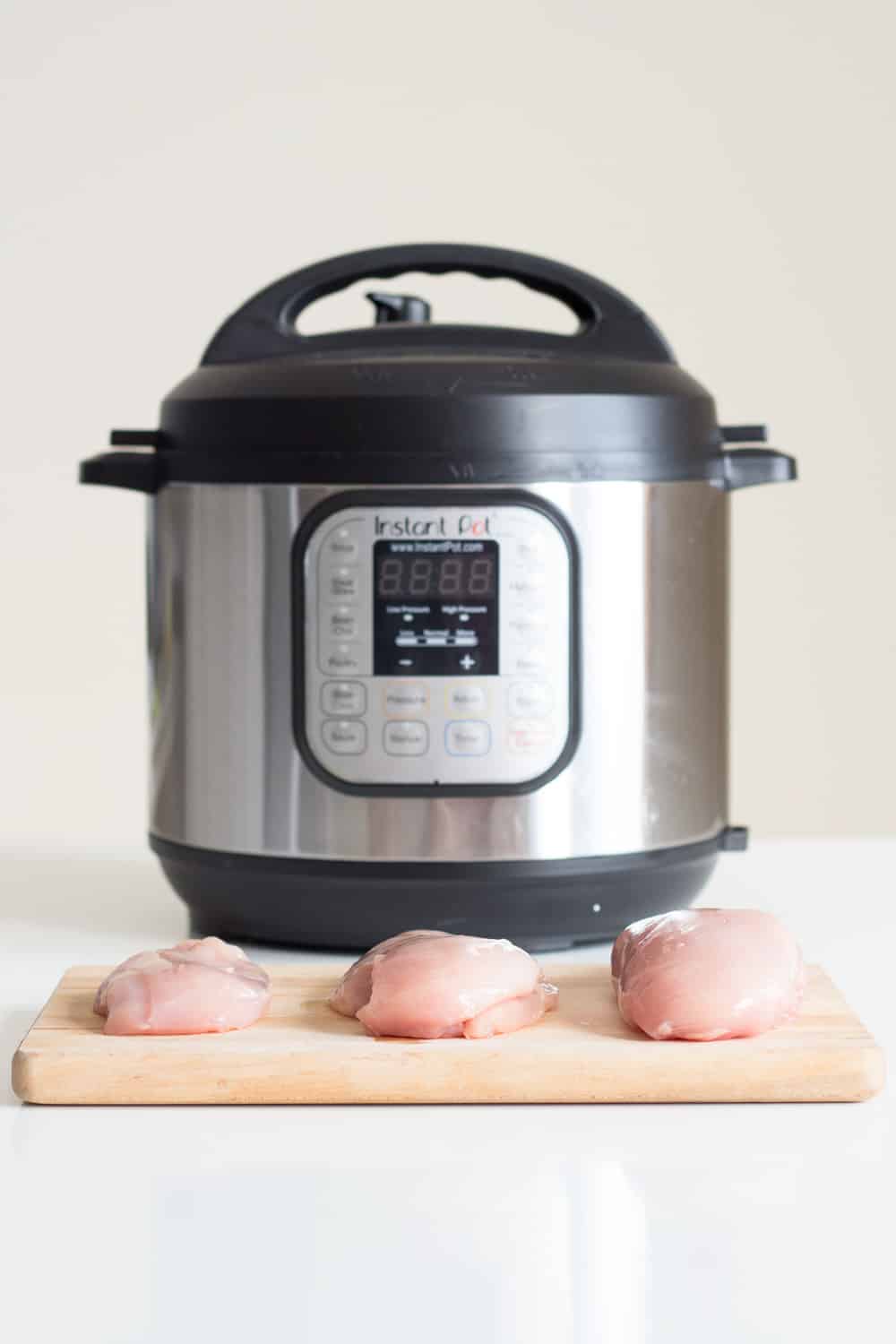 3 chicken breasts of different size on a cutting board in front of an Instant Pot