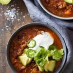 A bowl filled with chili con carne and topped with avocado, sour cream, jalapeno, and cilantro.
