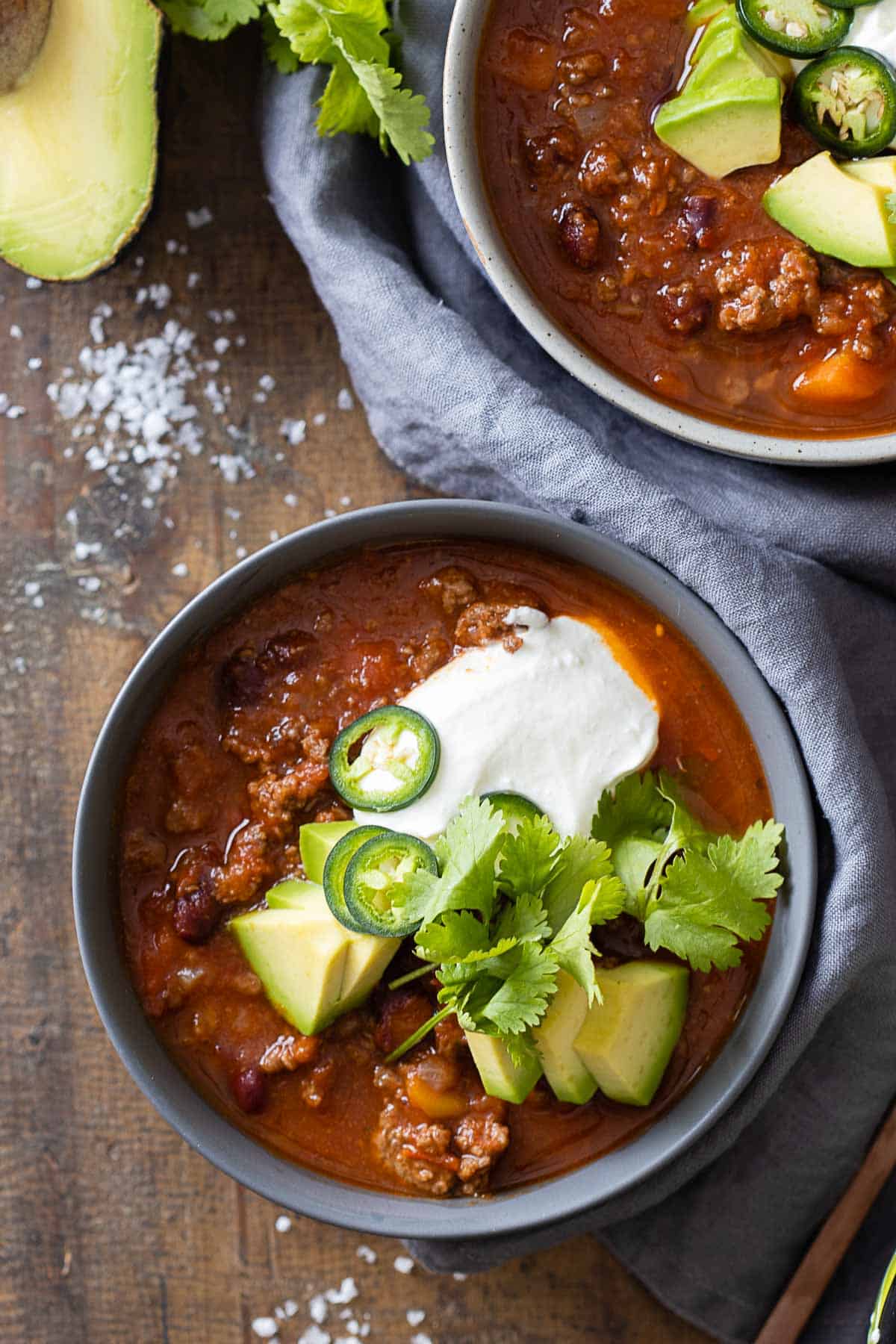 A bowl filled with chili con carne and topped with avocado, sour cream, jalapeno, and cilantro.